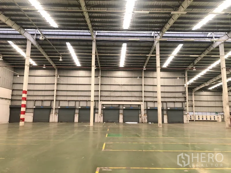 工厂 出租在Phra Nakhon Si Ayutthaya - 厂房内部朝向装卸门的视角，条形照明明亮均匀。