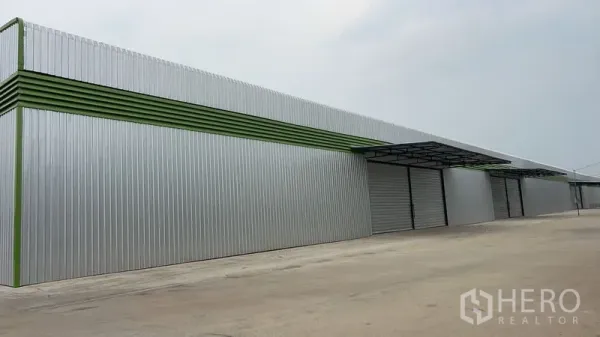 Warehouse for rent in Pathum Thani - Long steel-clad warehouse exterior with multiple roller shutters and a wide concrete yard in Lat Lum Kaeo, Pathum Thani.