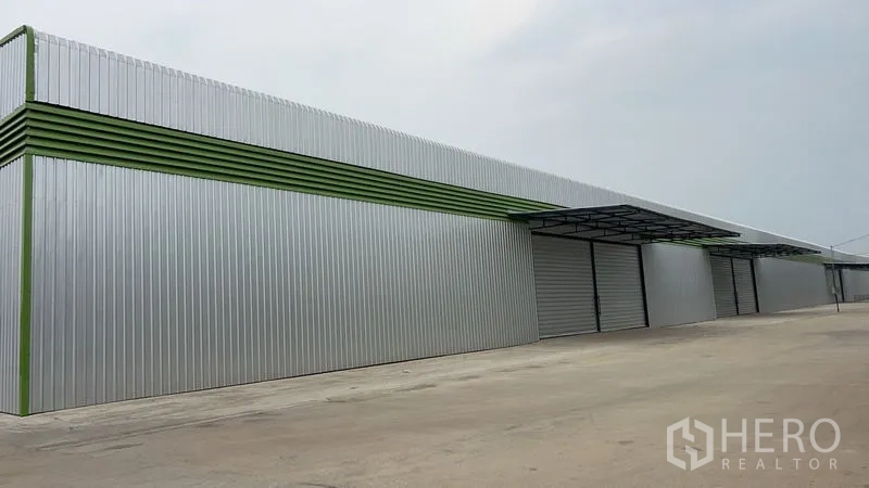 Warehouse for rent in Pathum Thani - Long steel-clad warehouse exterior with multiple roller shutters and a wide concrete yard in Lat Lum Kaeo, Pathum Thani.