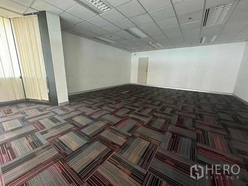 Office Space for rent in Khlong Toei, Bangkok - Empty office room with patterned carpet tiles and grid ceiling lights.