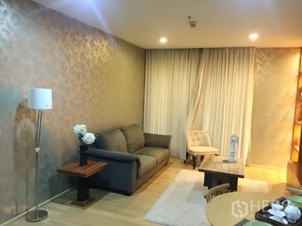 Condominium for rent in Watthana, Bangkok - Cozy living room with gray sofa, floor lamp, coffee table, and full-height curtains on wood floors.