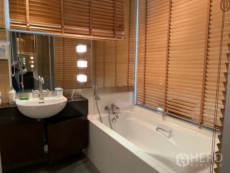 Condominium for rent - Contemporary bathroom with soaking tub, vanity, and wooden blinds around a large mirror.