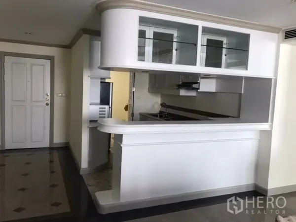 Condominium for rent in Watthana, Bangkok - Semi‑open kitchen with white breakfast bar, overhead glass cabinets and stainless appliances.