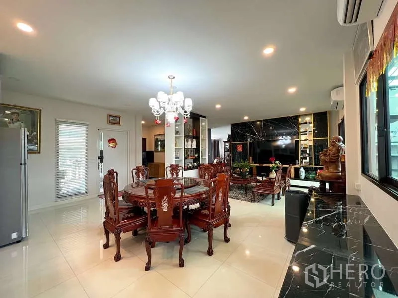 Detached House for sale in Prawet, Bangkok - Open-plan dining and living space with crystal chandelier, round table, and marble TV feature wall.