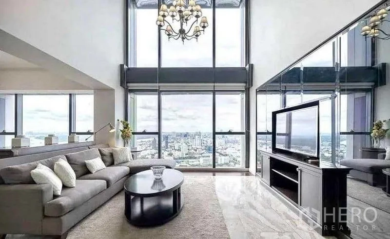 Condominium for rent - Double-height living room with floor-to-ceiling windows, chandelier and panoramic Bangkok skyline.