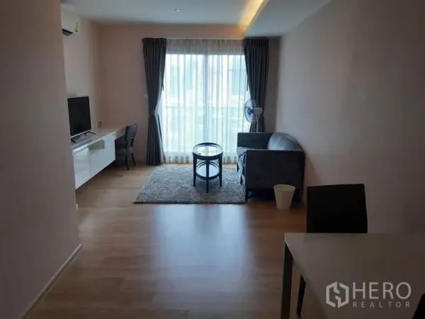 Condominium for rent or sale in Watthana, Bangkok - Bright living room with floor-to-ceiling window, TV console, desk and sofa.