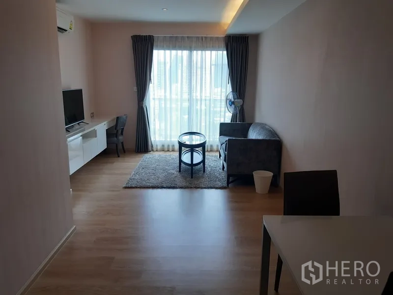 Condominium for rent or sale in Watthana, Bangkok - Bright living room with floor-to-ceiling window, TV console, desk and sofa.