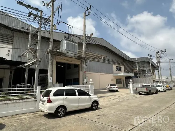 工厂 出租在Samut Prakan - 工厂外立面侧视，沿工业街道，设变压器、高挑装卸口和架空电缆。