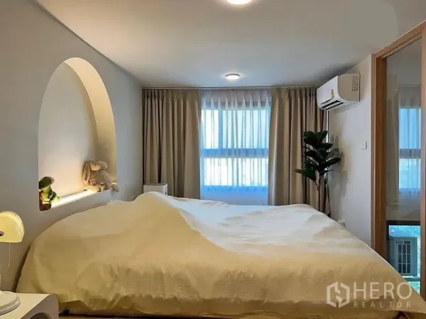 คอนโด ให้เช่าในHuai Khwang, Bangkok - ห้องนอนสว่างพร้อมหัวเตียงเว้าทรงโค้ง มีหน้าต่างบานใหญ่ ผ้าม่าน และแอร์ผนัง