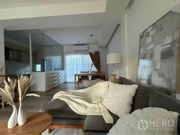 Detached House for rent in Prawet, Bangkok - Bright open‑plan living room with sectional sofa, dining area and a glass‑partition kitchen.