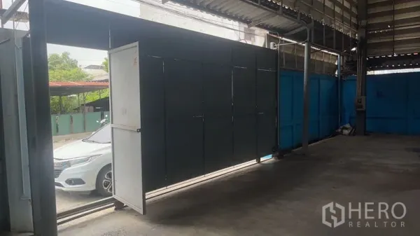 Warehouse for rent in Bang Na, Bangkok - Large metal sliding gate at the covered warehouse entrance for truck access, with a car visible outside.
