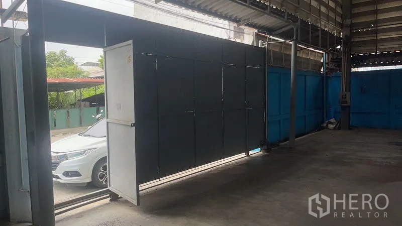 Warehouse for rent in Bang Na, Bangkok - Large metal sliding gate at the covered warehouse entrance for truck access, with a car visible outside.