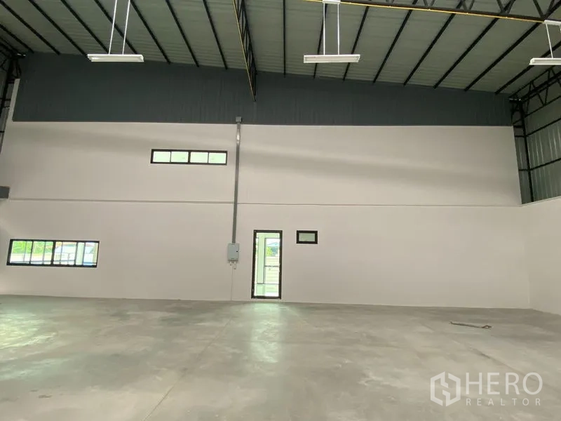 Warehouse for rent or sale in Bang Len, Nakhon Pathom - Interior wall with personnel door and windows beneath the tall roof.