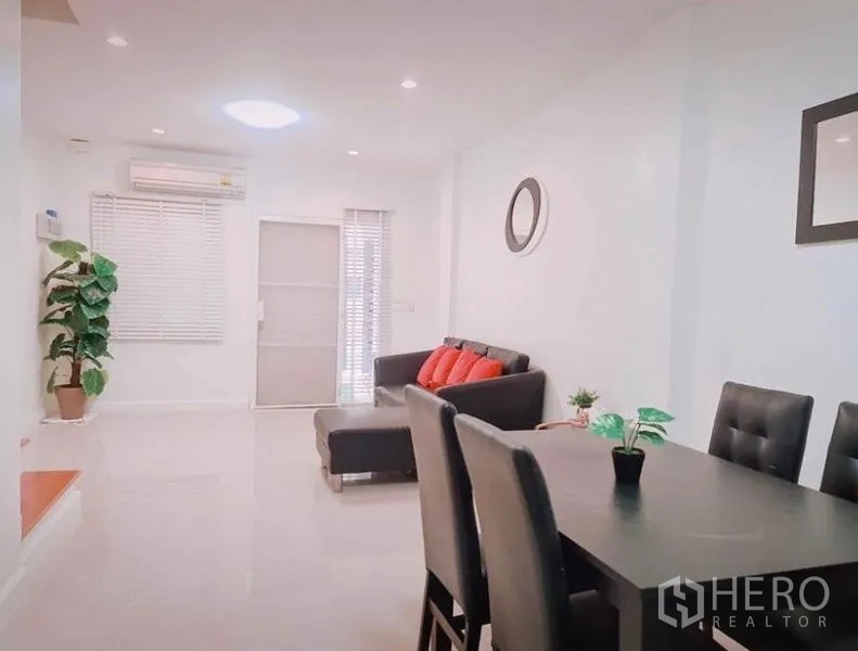 Townhouse for rent in Suan Luang, Bangkok - Open-plan dining and living area with black dining set and sectional sofa