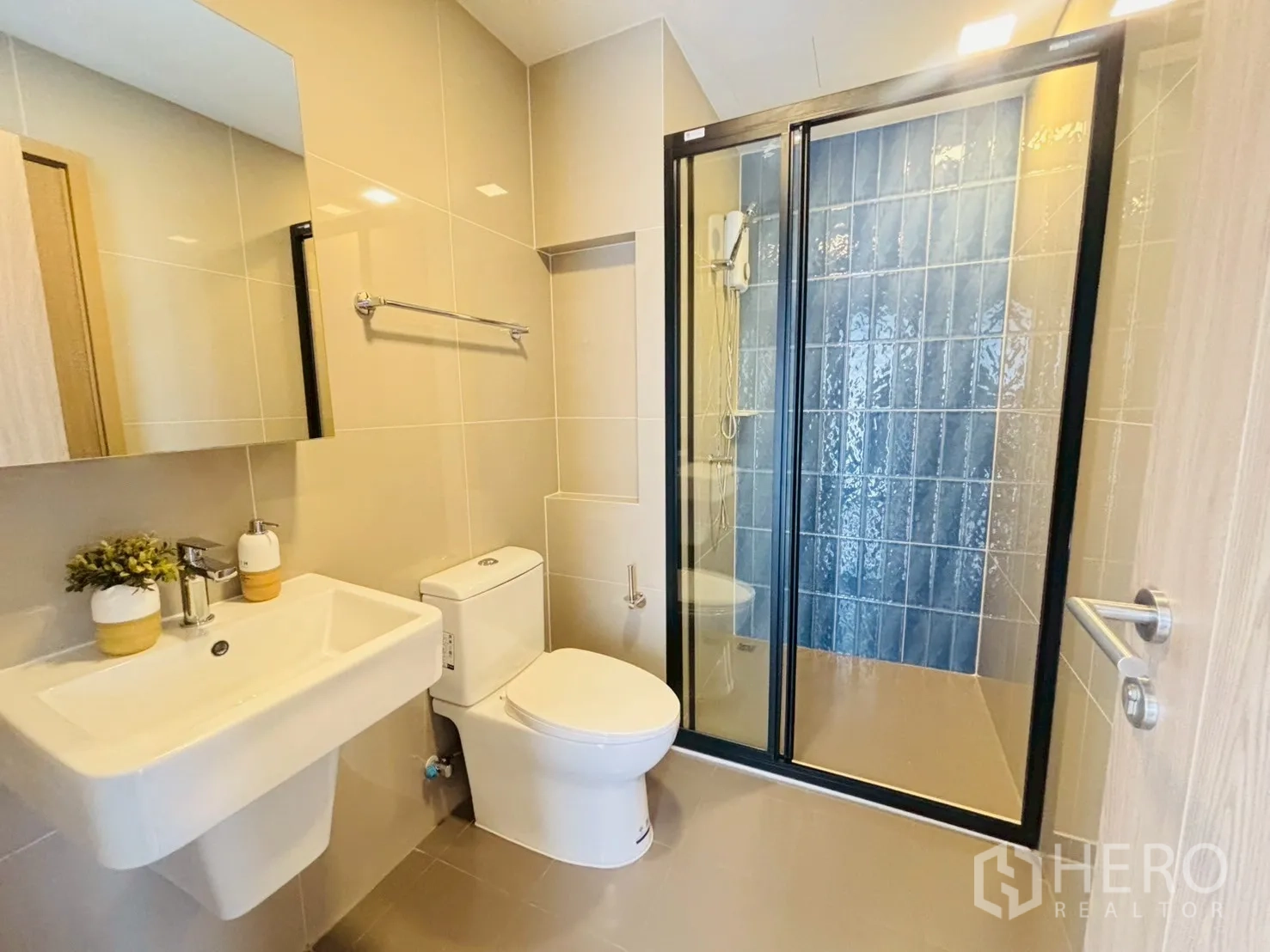 Condominium for rent in Watthana, Bangkok - Contemporary bathroom with glass-enclosed shower, toilet, and wall-mounted sink with mirror.