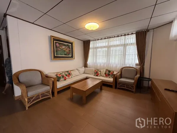 บ้าน ให้เช่าในPhra Khanong, Bangkok - ห้องนั่งเล่นอบอุ่น เก้าอี้หวาย โซฟาเข้ามุม โต๊ะไม้ และผ้าม่านหน้าต่าง.