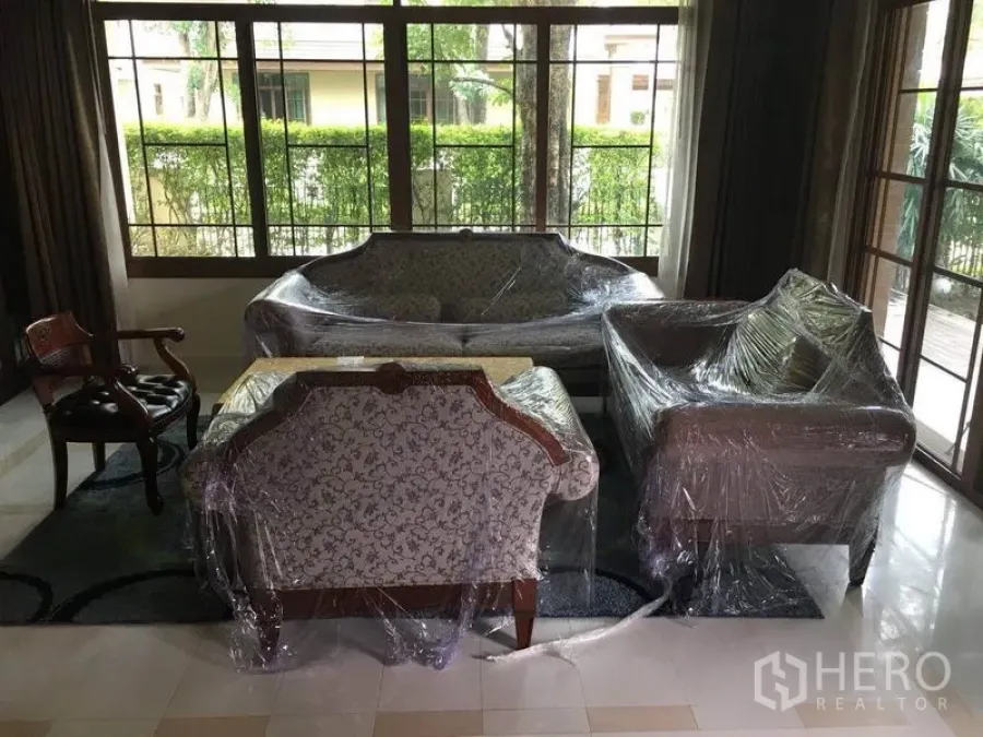 Detached House for rent in Bang Phli, Samut Prakan - Bright living room with classic sofas wrapped for protection and large windows facing a green hedge.