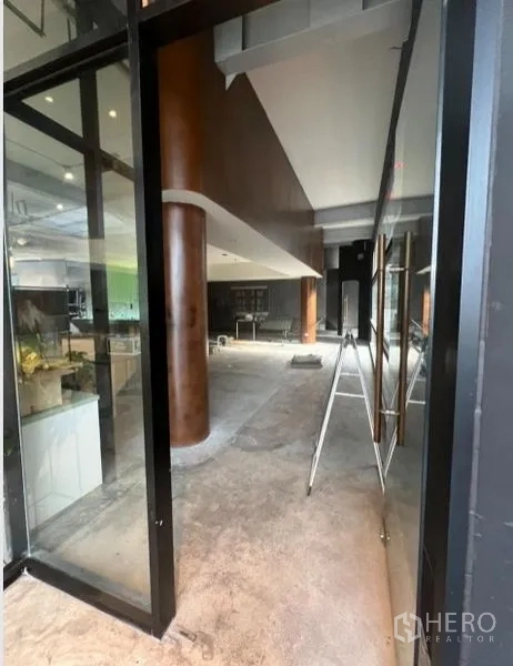 零售空间 出租在Watthana, Bangkok - 玻璃入口与店面立面，内部空间宽阔并带木饰圆柱。