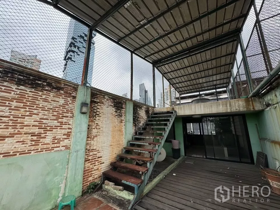 店屋 出租在Bang Rak, Bangkok - 屋顶露台带金属楼梯与顶棚，砖墙外可见城市天际线。