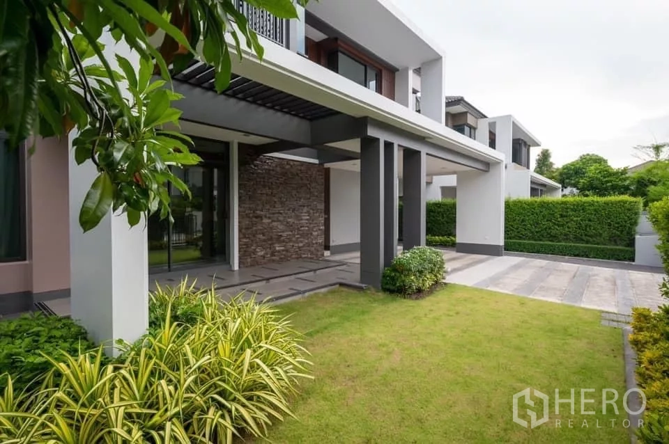 บ้าน ให้เช่าในPrawet, Bangkok - มุมมองด้านข้างของตัวบ้าน ผนังตกแต่งหิน สนามหญ้า และทางจอดรถปูพื้น