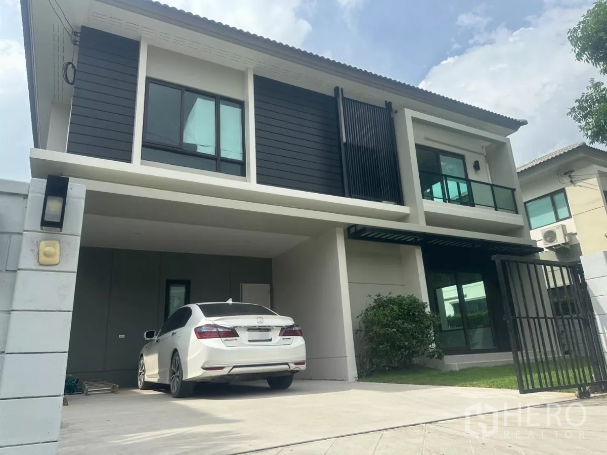 Detached House for sale in Samut Prakan - Two-storey detached house with modern facade, covered two-car carport, gate and small front lawn.