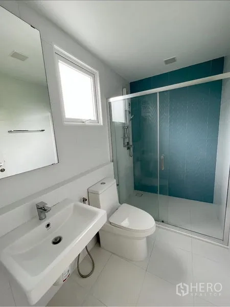 Detached House for rent or sale in Prawet, Bangkok - Bathroom with glass shower enclosure, blue accent wall and window.