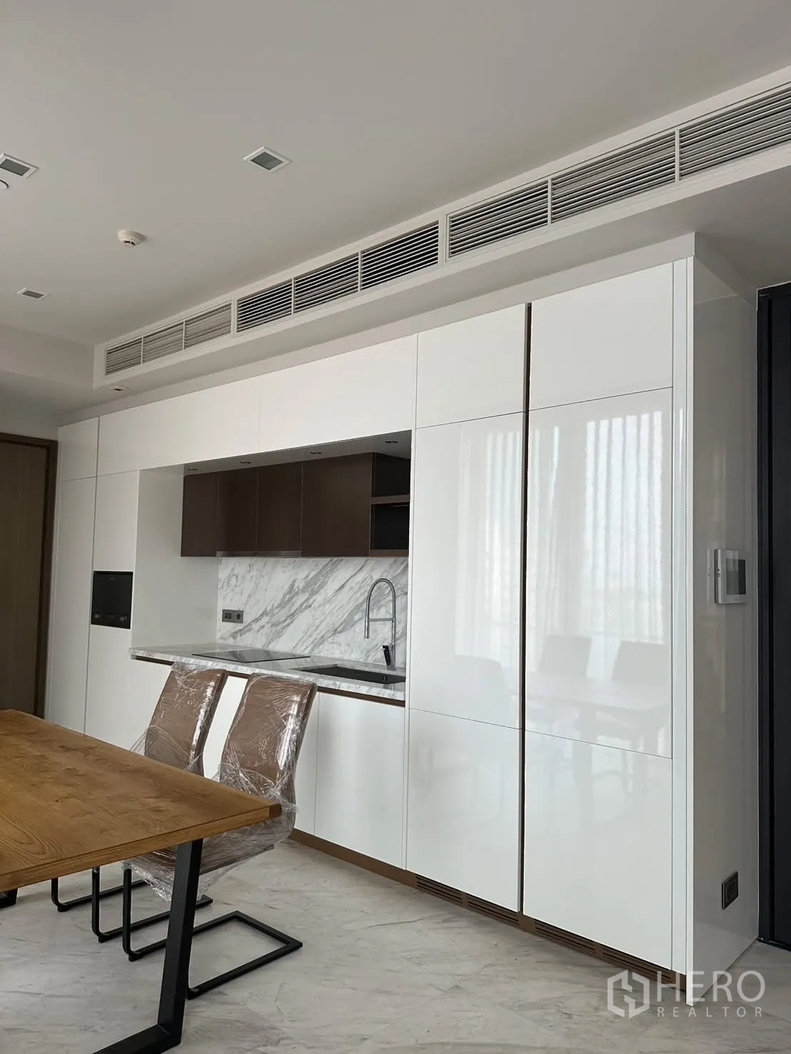 Condominium for rent or sale in Watthana, Bangkok - Modern kitchenette with glossy white cabinetry and marble backsplash.