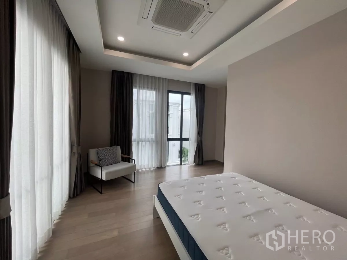 Detached House for rent in Lat Phrao, Bangkok - Large secondary bedroom with wide windows, light wood floors and simple furnishings.