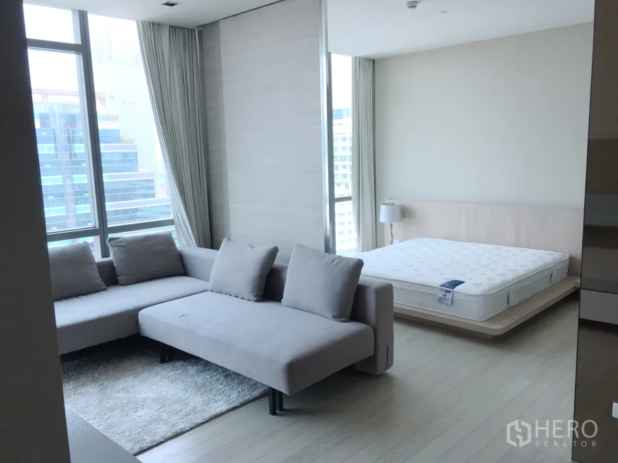 公寓 出租或出售在Watthana, Bangkok - 明亮的开放式起居与睡眠区，L形沙发、平台床与落地窗城市景观。