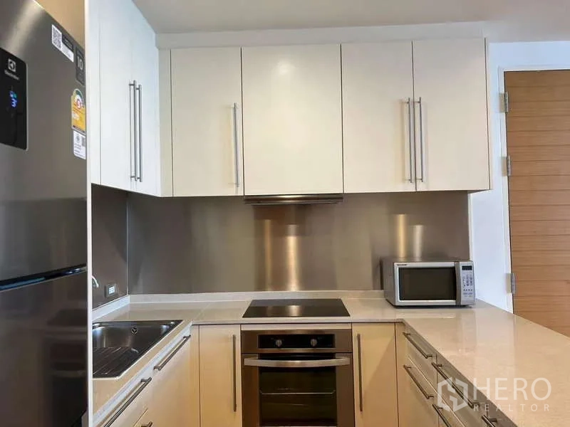 Condominium for rent in Bang Kho Laem, Bangkok - U-shaped kitchen with oven, cooktop, and stainless backsplash.