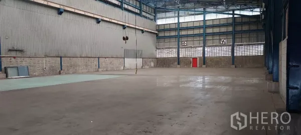 货栈 出租在Mueang Samut Prakan, Samut Prakan - 宽阔混凝土地面，钢墙通风口与红色安全门。