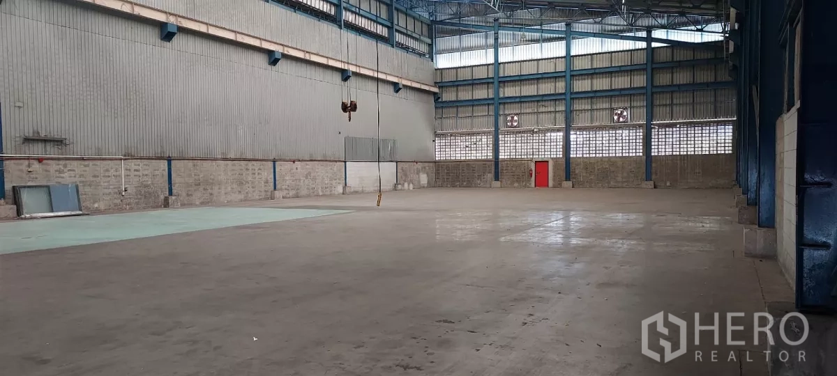 货栈 出租在Mueang Samut Prakan, Samut Prakan - 宽阔混凝土地面，钢墙通风口与红色安全门。