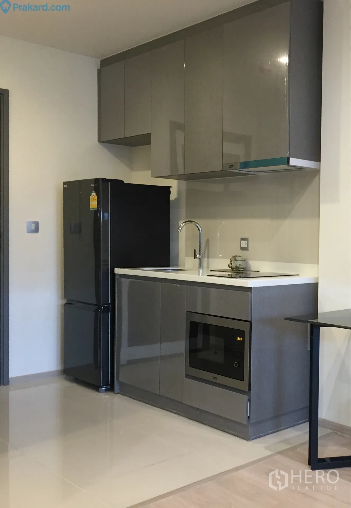Condominium for rent in Ratchathewi, Bangkok - Sleek kitchenette with glossy grey cabinets, sink, induction hob, microwave and black fridge.