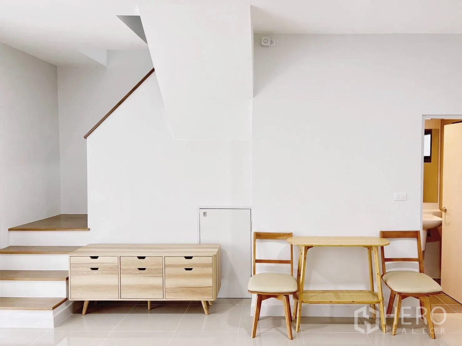 ทาวน์เฮาส์ for rent in Bang Phli, Samut Prakan - ผนังบันไดพร้อมตู้คอนโซลไม้และชุดโต๊ะเล็กกับเก้าอี้ โดยมีประตูห้องน้ำด้านข้าง.