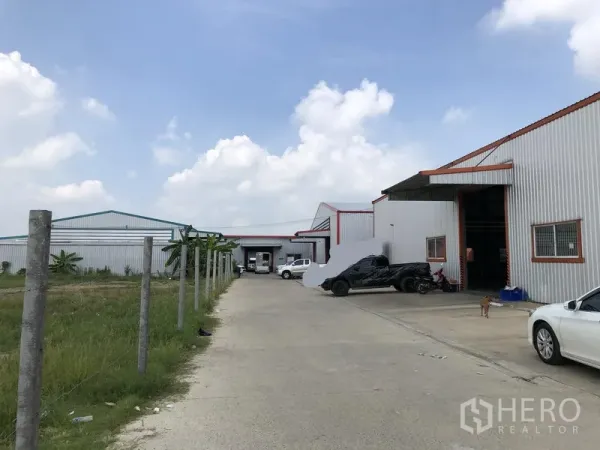 Warehouse for rent in Nonthaburi - Concrete access road between warehouse buildings with adjacent grassy plot and perimeter posts.