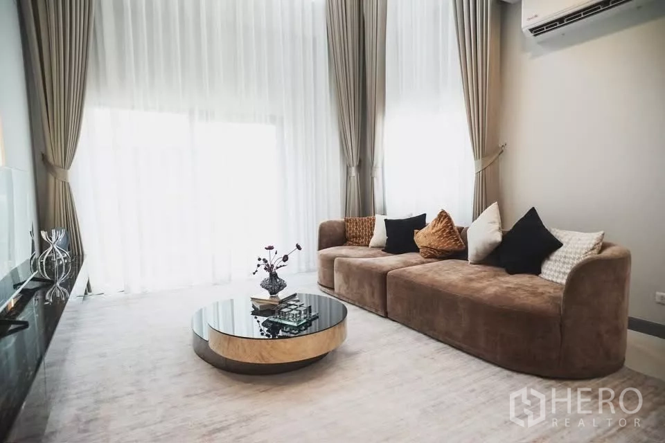 Detached House for rent in Bang Phli, Samut Prakan - Bright living area with floor-to-ceiling sheer curtains, plush sofa and round glass coffee table.