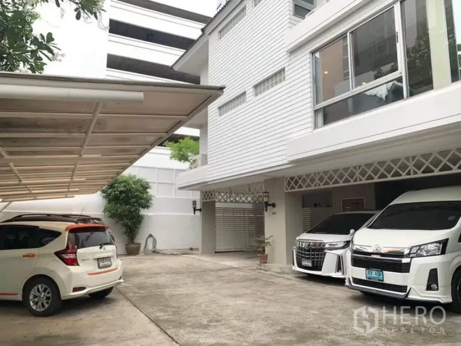 ทาวน์เฮาส์ ให้เช่าในKhlong Toei, Bangkok - ลานหน้าบ้านของทาวน์เฮ้าส์สีขาวหลายชั้นพร้อมที่จอดรถมีหลังคาและรถจอด