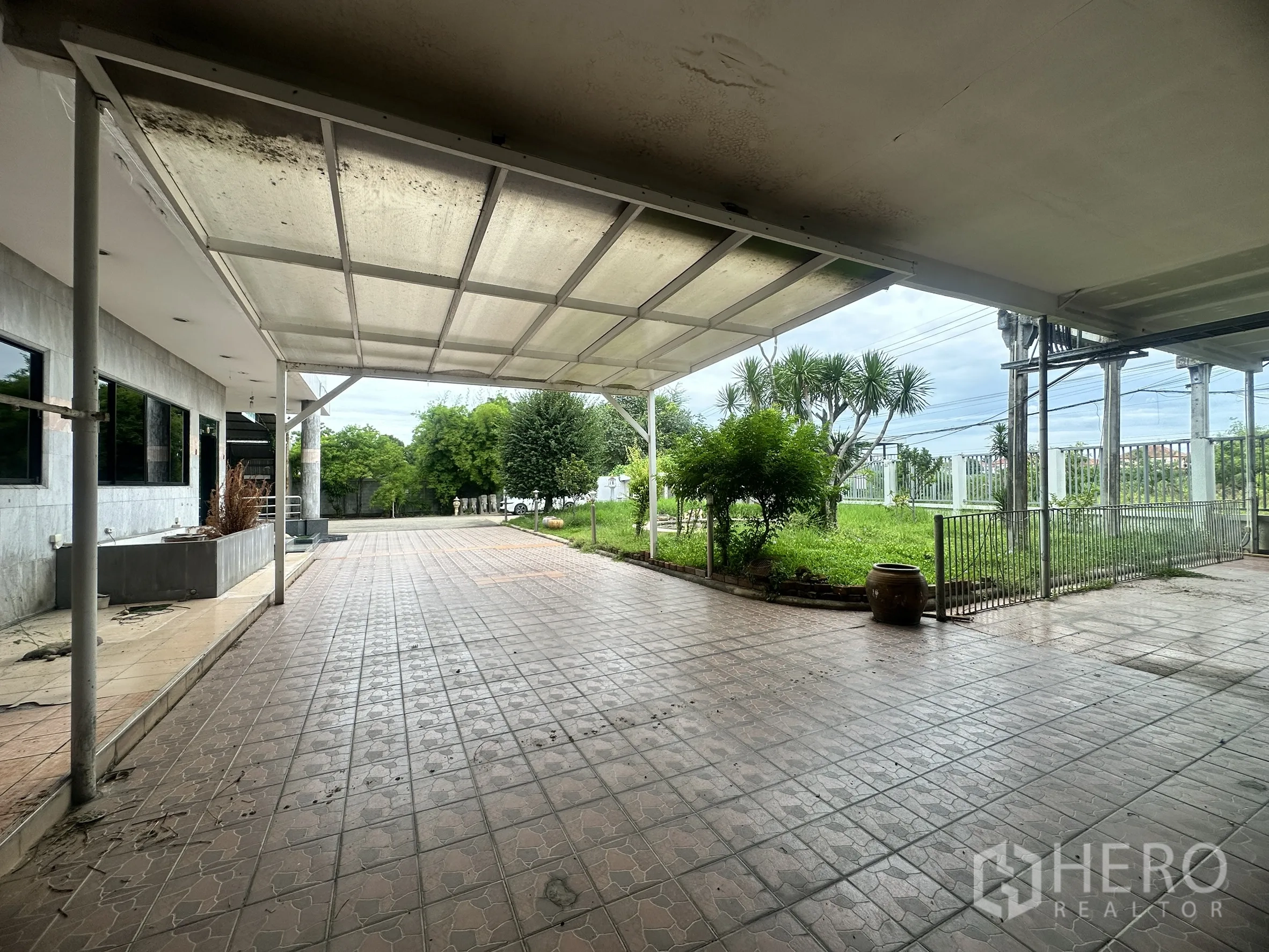 Factory for sale in Bang Bua Thong, Nonthaburi - Covered terrace with tiled driveway beside a landscaped garden and perimeter fence.