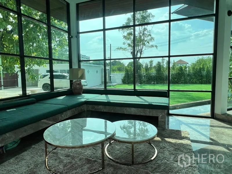 Detached House for sale in Prawet, Bangkok - Sunroom with floor-to-ceiling windows overlooking green lawn and driveway.