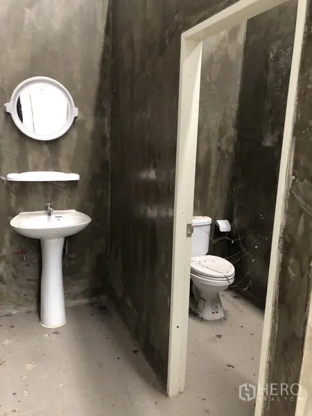Warehouse for rent in Lat Lum Kaeo, Pathum Thani - On-site restroom with pedestal sink, mirror and toilet set against cement-finish walls.