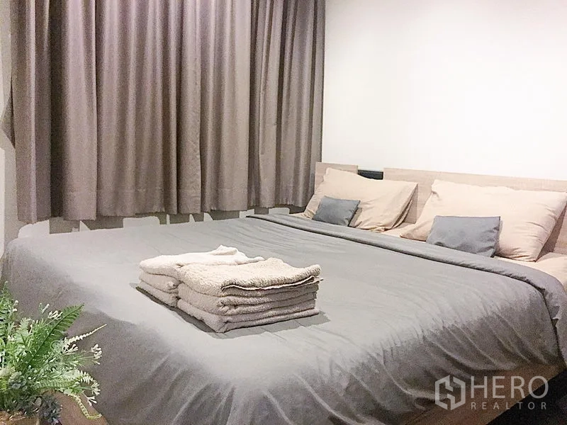 公寓 出租在Watthana, Bangkok - 温馨卧室，灰色床品与多层靠枕，搭配全遮光窗帘。