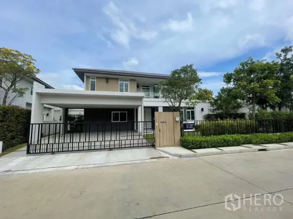Detached House for rent or sale in Bang Bua Thong, Nonthaburi - Modern two-storey detached house with gated double carport and landscaped front garden on a quiet estate street.