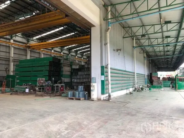 工厂 出租或出售在Lat Lum Kaeo, Pathum Thani - 高挑厂房仓库，配行车吊与成排绿色材料，旁设有有顶装卸区。