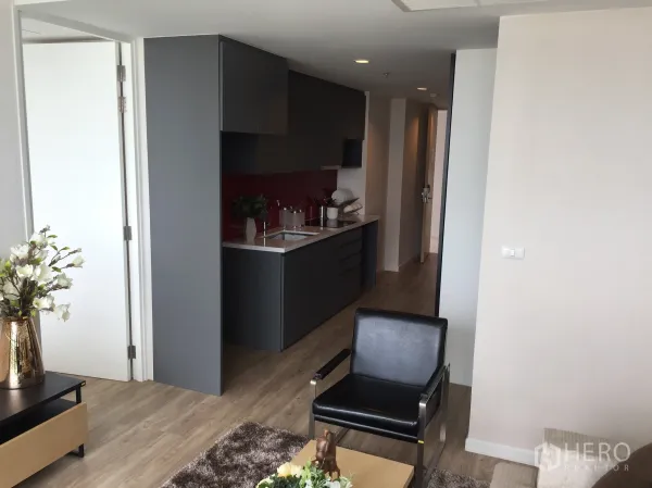 公寓 出售在Bang Rak, Bangkok - 客厅连通灰色一字型厨房，红色挡板与木地板，现代公寓。