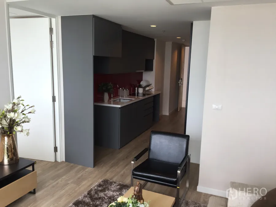 公寓 出售在Bang Rak, Bangkok - 客厅连通灰色一字型厨房，红色挡板与木地板，现代公寓。