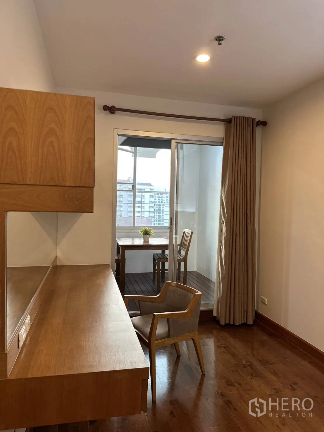 Condominium for rent in Watthana, Bangkok - Study nook with long wooden built-in desk and chair opening to a balcony seating area.