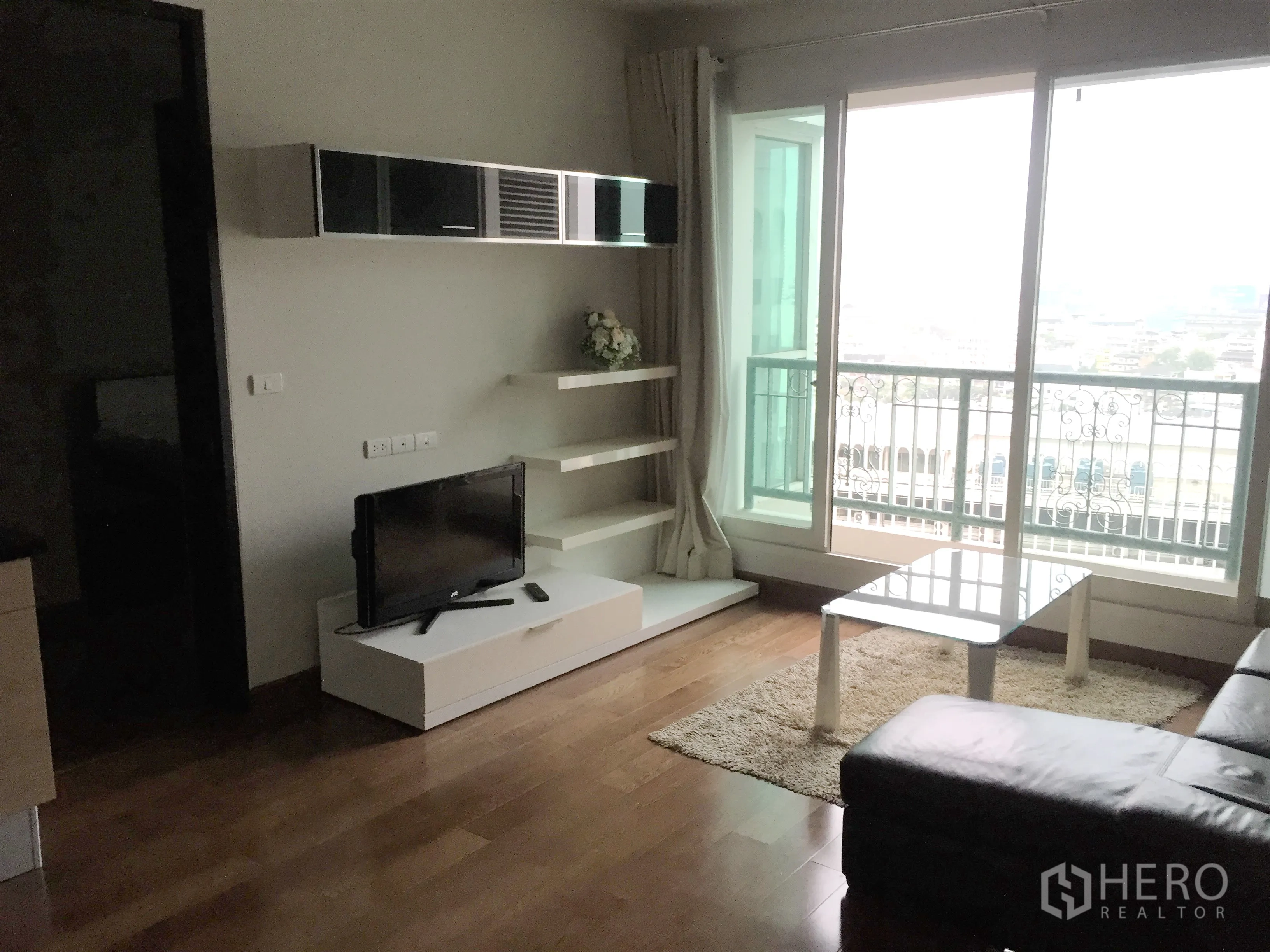 คอนโด ให้เช่าหรือขายในPathum Wan, Bangkok - ห้องนั่งเล่นสว่างโปร่ง กระจกเต็มบาน พร้อมระเบียงวิวเมือง พื้นไม้ และชั้นวางทีวี