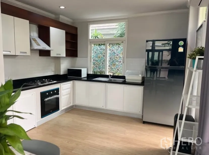 独立式住宅 出租或出售在Lat Phrao, Bangkok - L形厨房，白色橱柜黑色台面，配烤箱、炉灶、油烟机和冰箱。