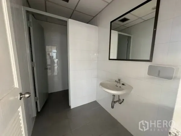办公空间 出租在Bang Rak, Bangkok - 办公室内洁白瓷砖卫浴，挂墙式洗手盆、镜子与独立隔间。