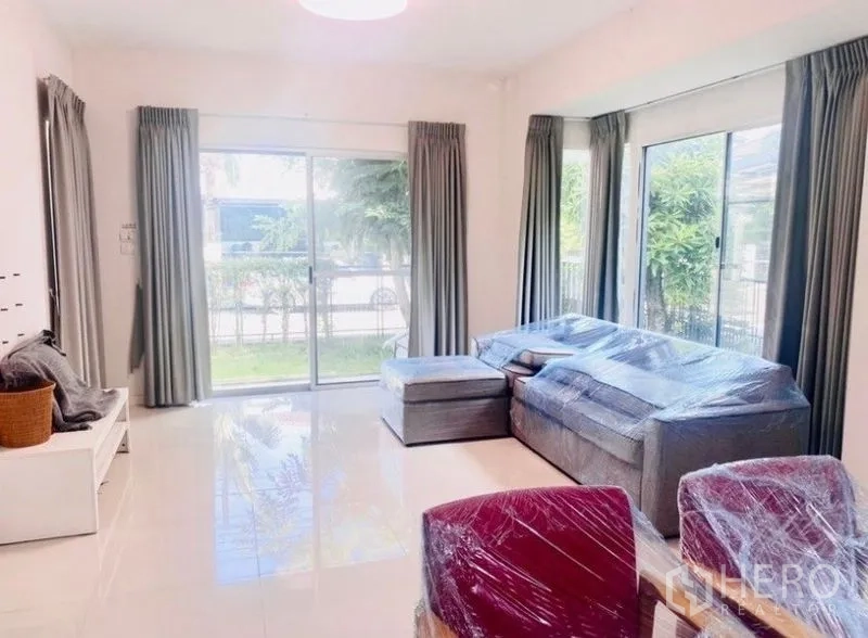 Detached House for rent or sale - Bright living room with sliding glass doors, large windows, gray curtains and an L‑shaped sofa on glossy tile flooring.